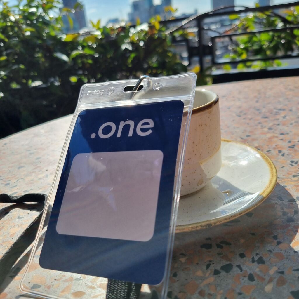 A Dot One Conference Pass leans casually against a coffee mug, the London skyline stretching across the background in soft morning light.